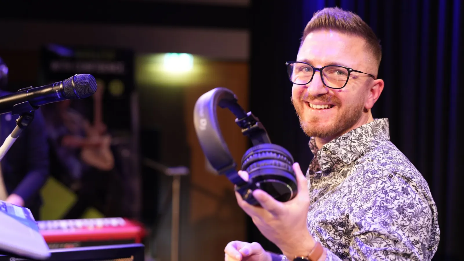 DJ Kevin von TK Motion lacht mit Kopfhörern in der Hand auf der Bühne